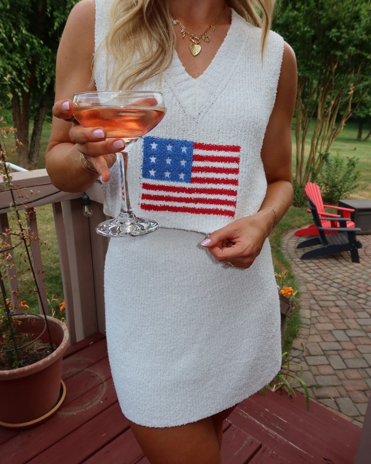 Woman in a white sleeveless dress with an American flag print holding a glass of rose wine.
