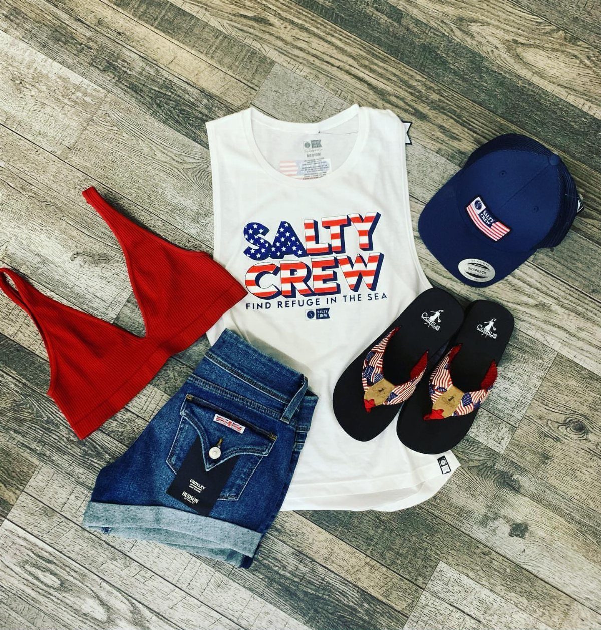Flat lay of summer clothing including a white tank top, denim shorts, and patriotic accessories.
