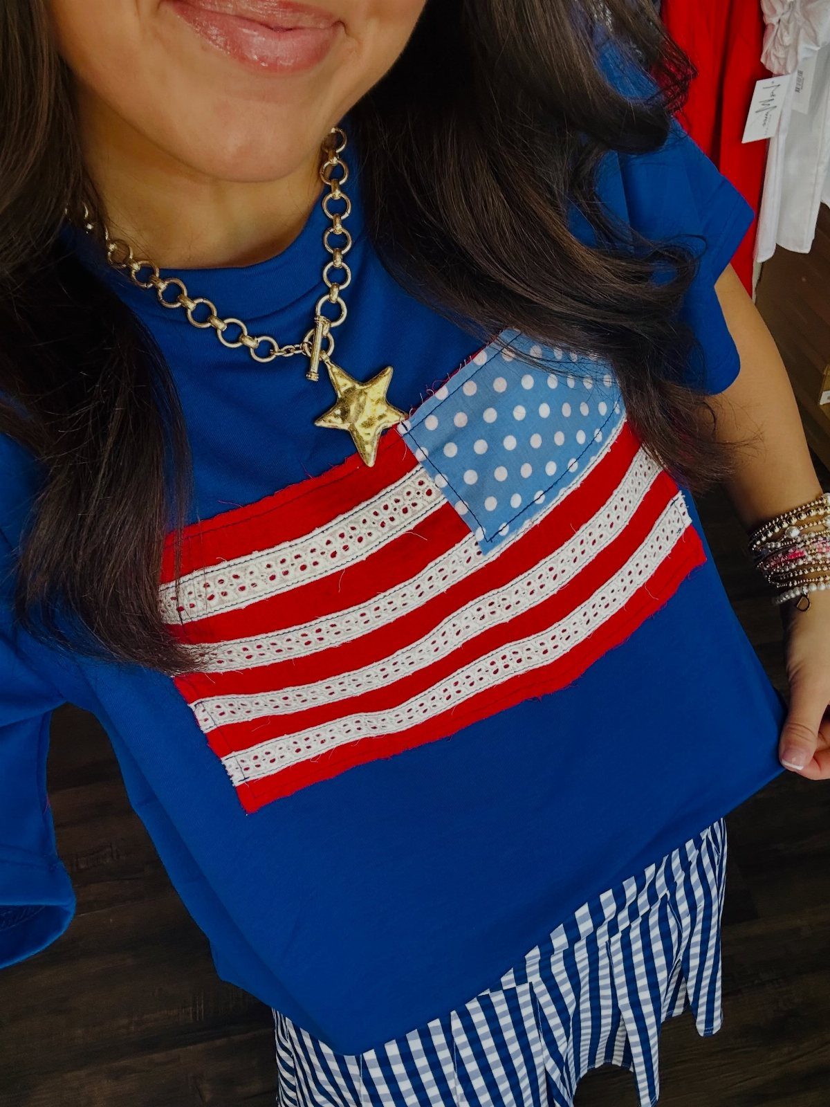 A person wearing a blue t-shirt with an American flag design and a gold star necklace.