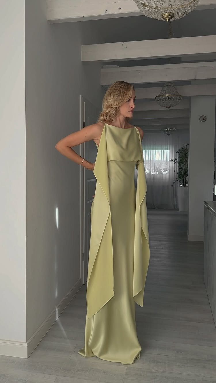 Blonde woman posing in a long, pale yellow sleeveless gown with flowing fabric panels.