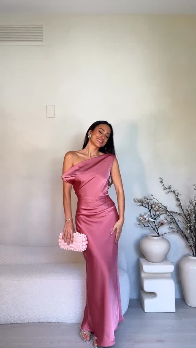 Woman wearing a long pink satin one-shoulder dress and holding a pink clutch.