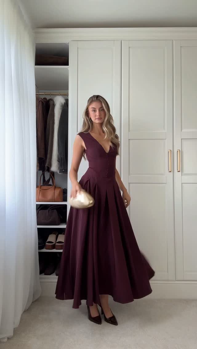 Woman in a burgundy sleeveless midi dress posing in a room with white wardrobes.