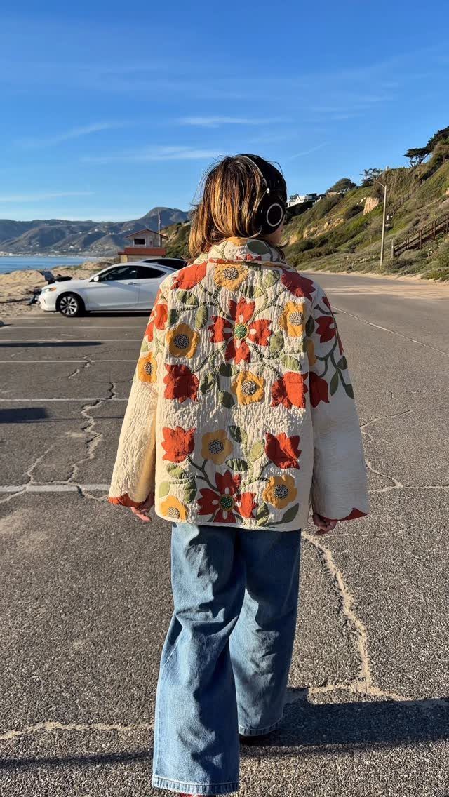 A person wearing a floral quilted jacket and wide-leg blue jeans walking outdoors.