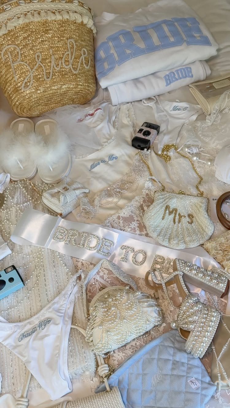 White and light blue bridal accessories including a sash, sweatshirt, and pearl-embellished items laid out.