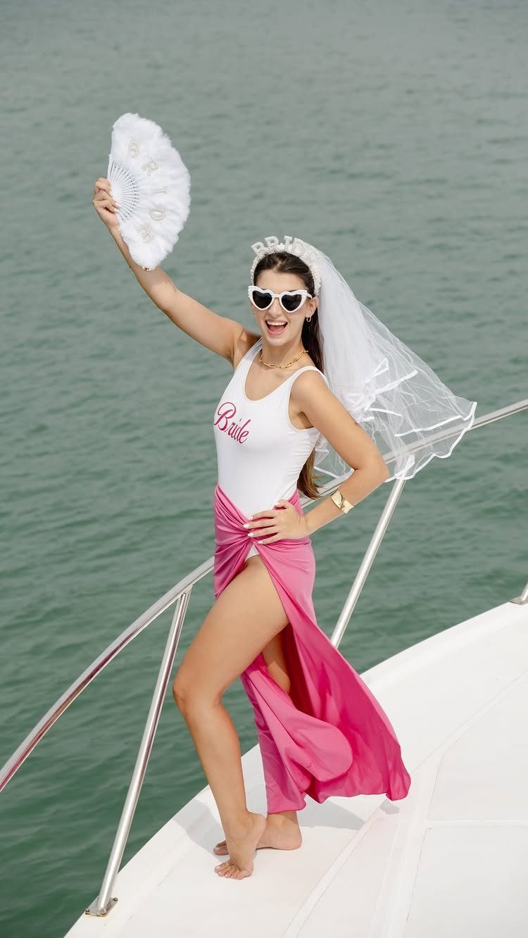 Smiling woman in a bride tank top, veil, and pink skirt posing on a boat.