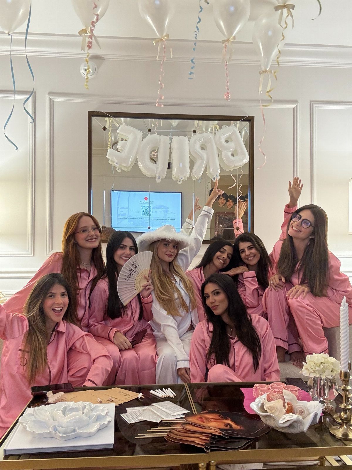Women in pink satin pajamas posing with a bride in white indoors.