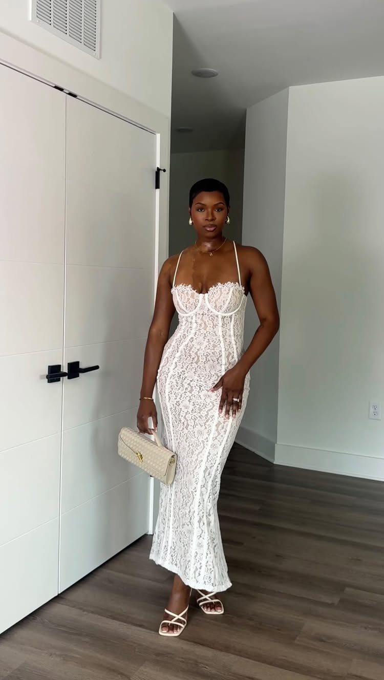 Woman posing in a white lace maxi dress and strappy sandals while holding a clutch.