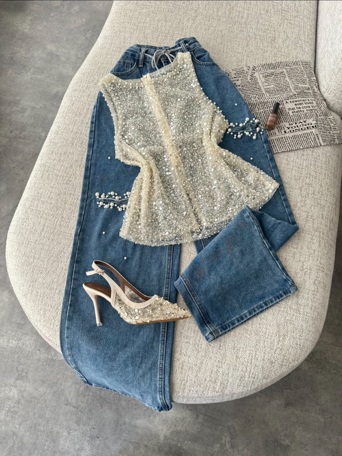 A sequined cream top laid over blue denim jeans with sparkly high heels on a chair.