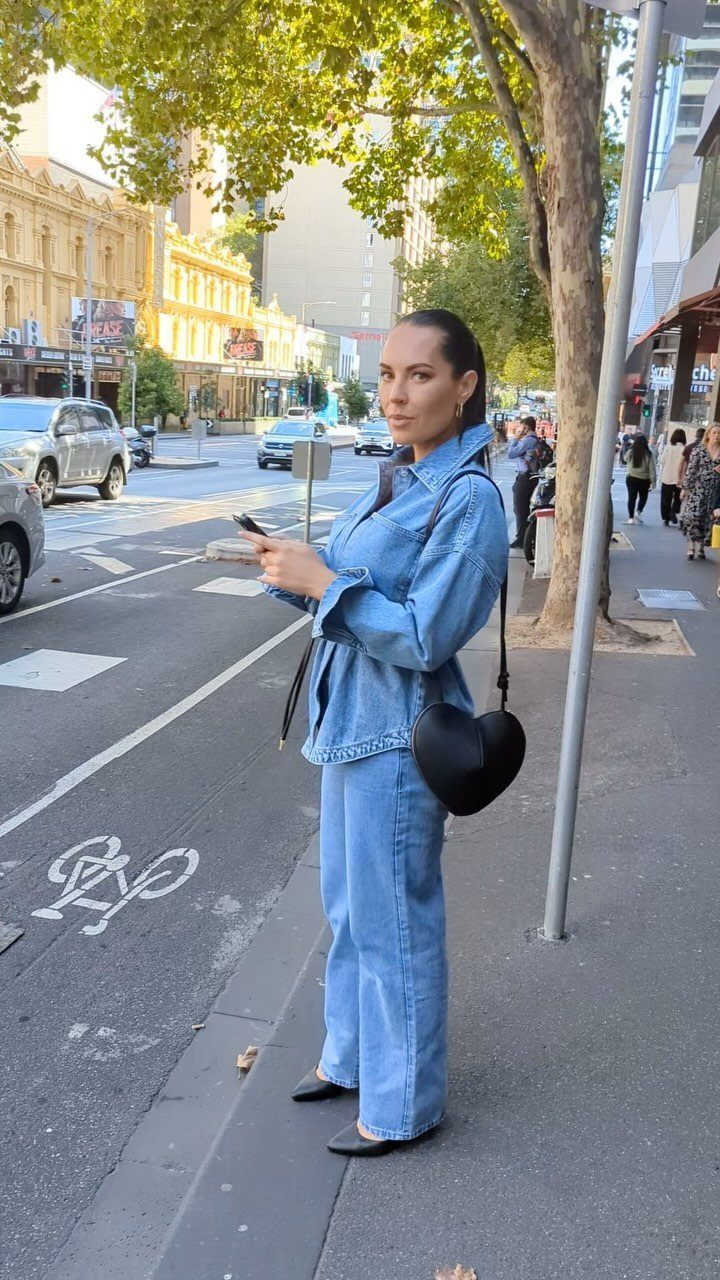 Woman standing on a city street wearing a denim button-up shirt and baggy jeans.