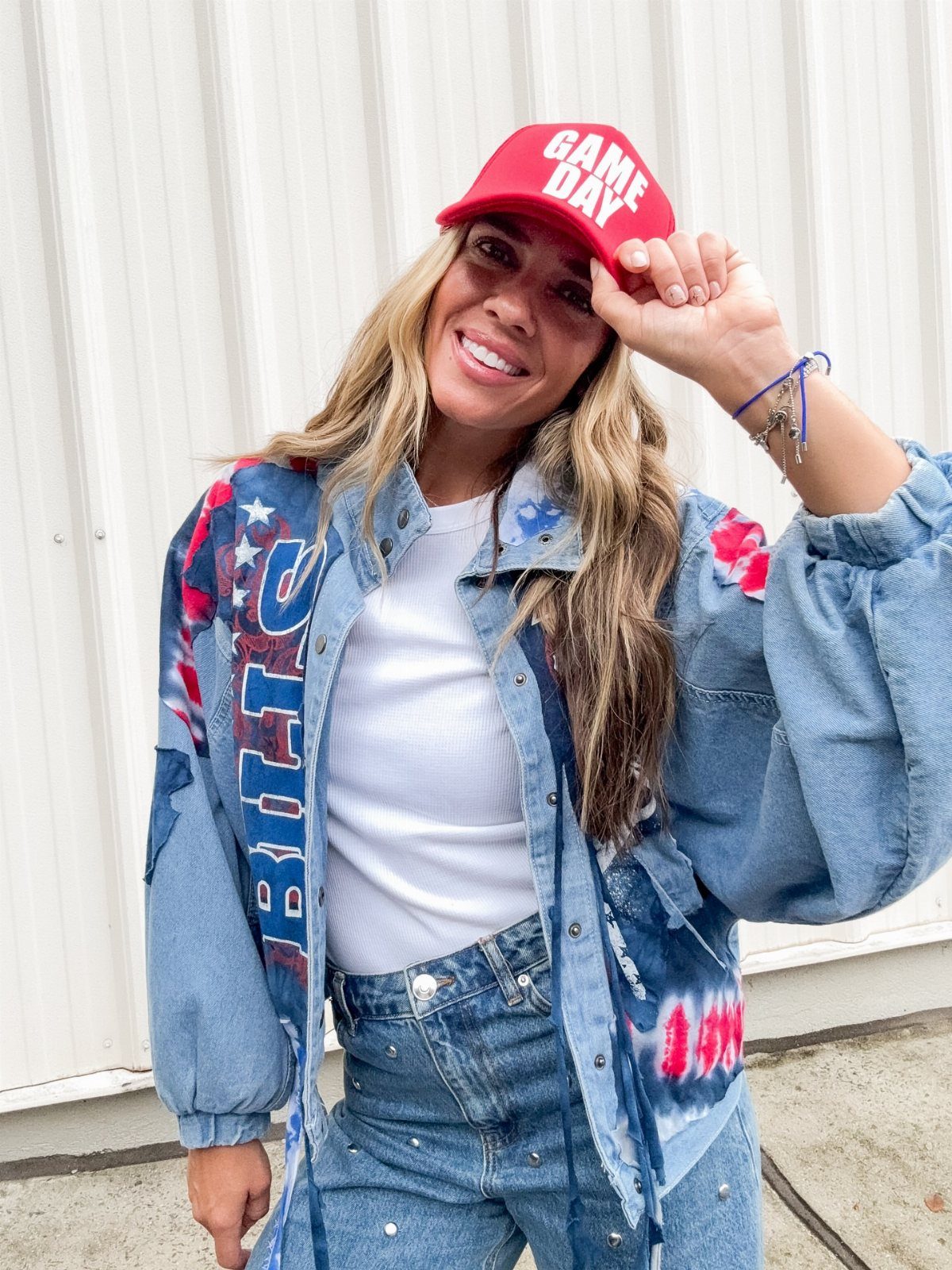 Smiling woman wearing a red game day cap and an oversized denim jacket over a white shirt.