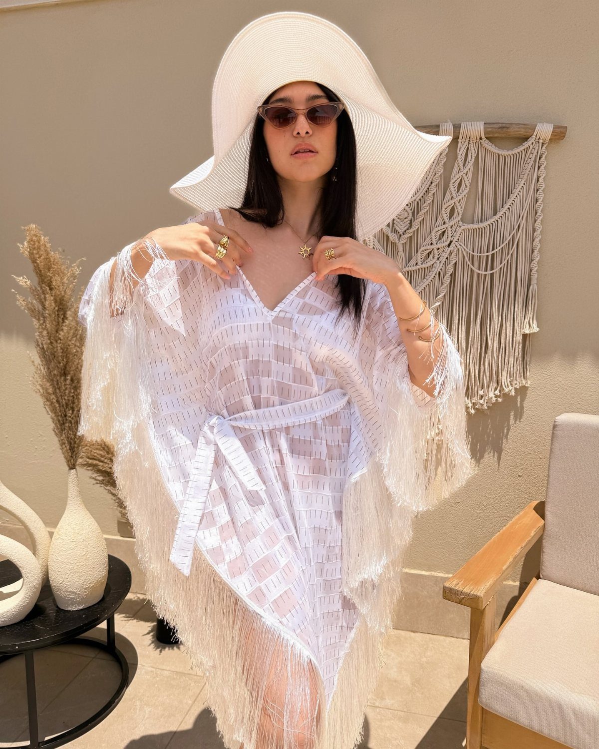 Woman wearing a large white sun hat and a white fringed lace cover-up over a swimsuit.