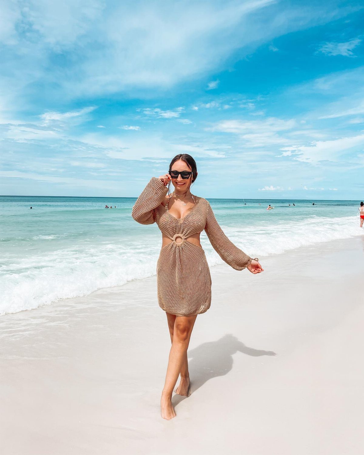 Woman in a brown crochet dress wearing sunglasses on a sunny tropical beach.