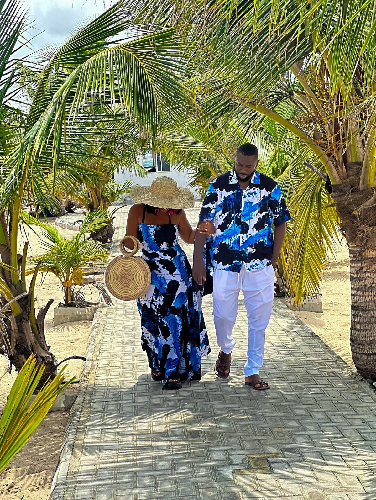 A couple walking through palm trees wearing matching blue and white tropical vacation outfits.