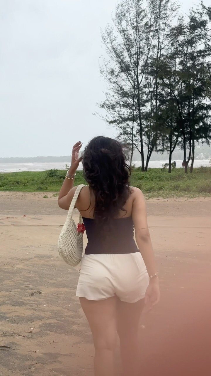 Woman walking on a sandy beach wearing white shorts and a black top.