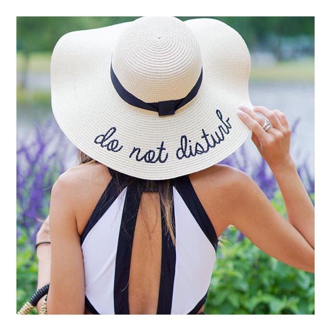 Woman wearing a large white straw sun hat with black embroidery and a black ribbon.