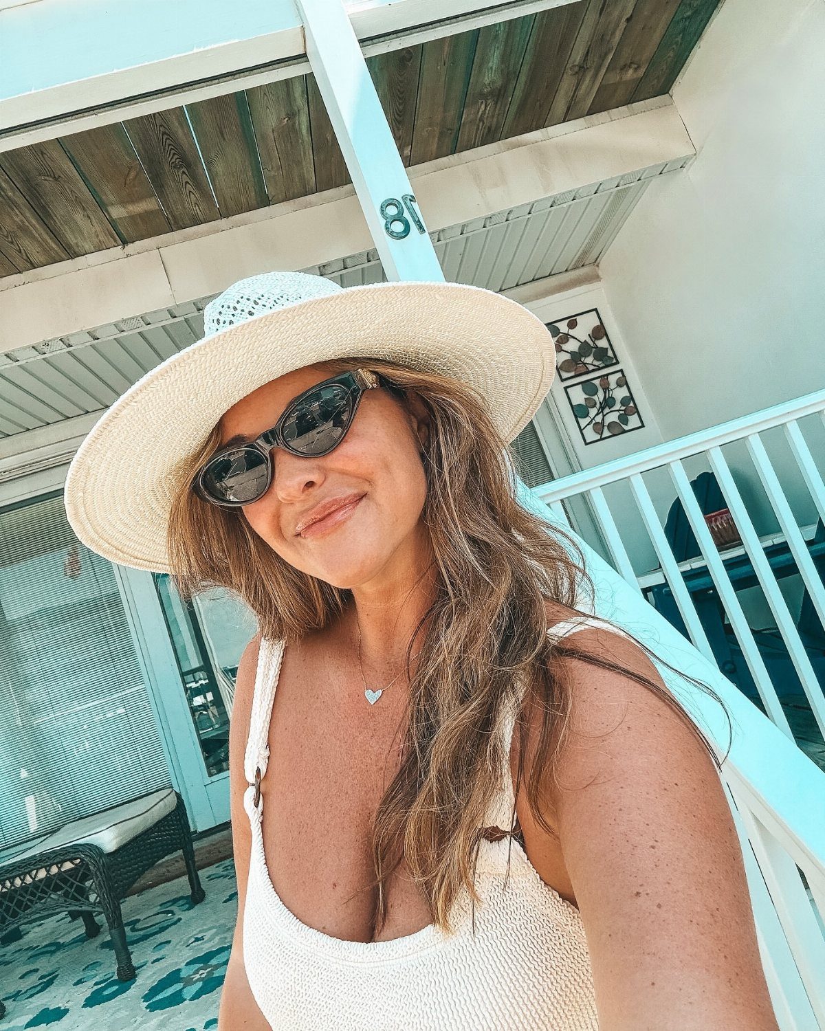 Smiling woman wearing a large white straw hat and dark oversized sunglasses outdoors.