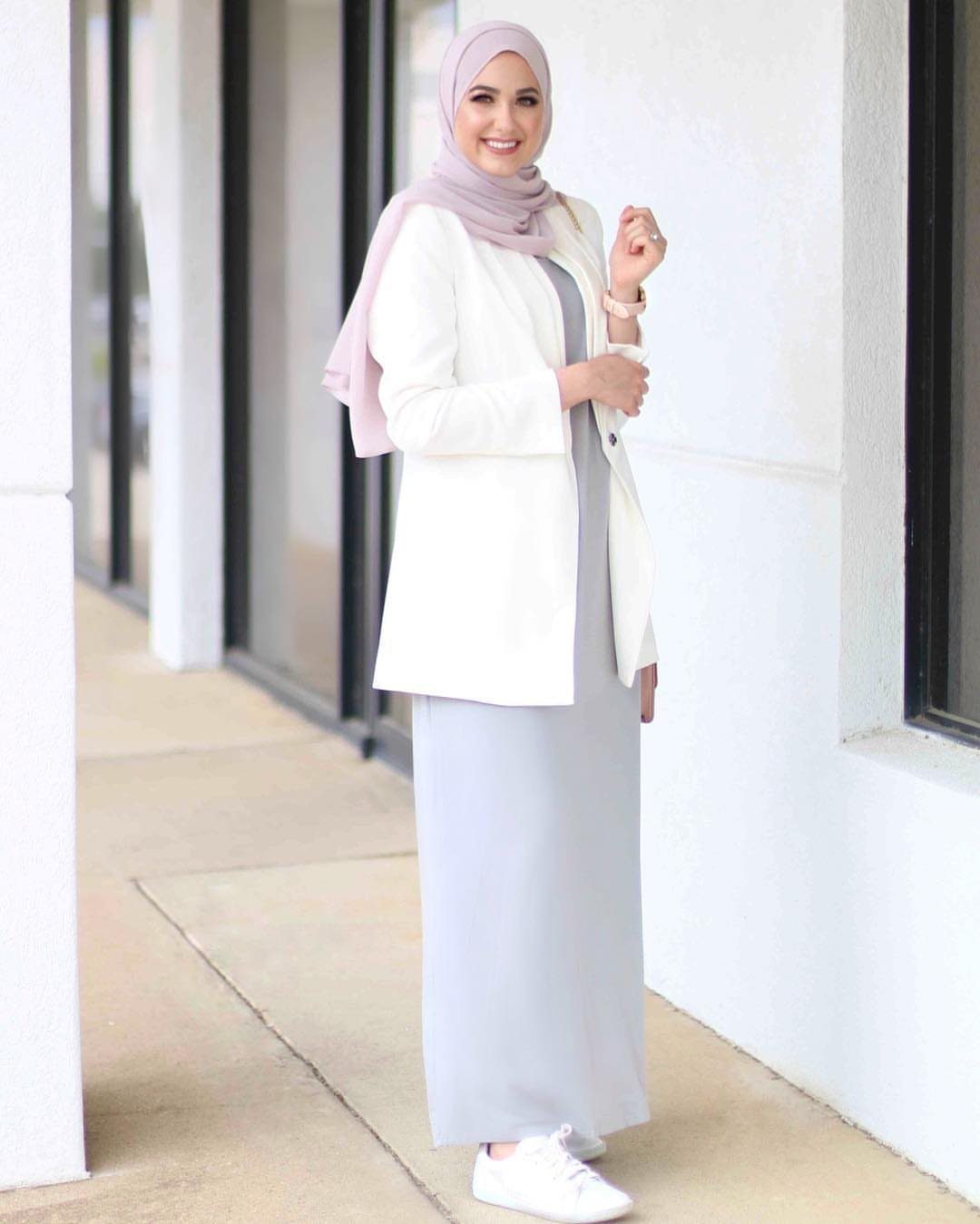 Woman in a white blazer and long grey maxi dress standing by white pillars.