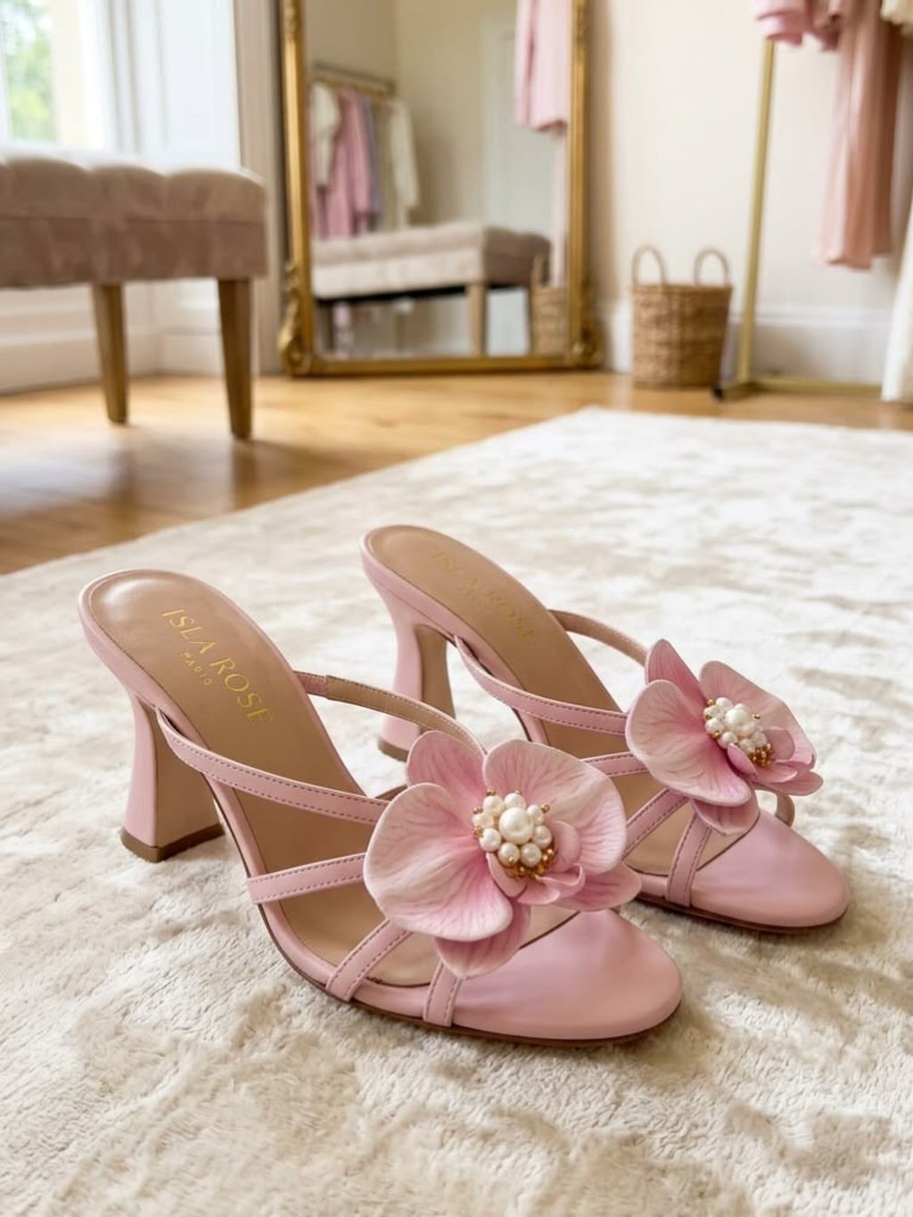 Pink strappy high heel sandals with large floral decorations and pearls on a white rug.