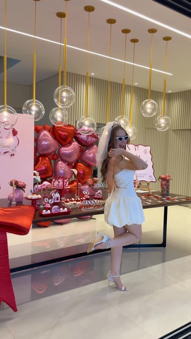 Woman in a white strapless mini dress and veil posing in front of a heart-themed dessert table.