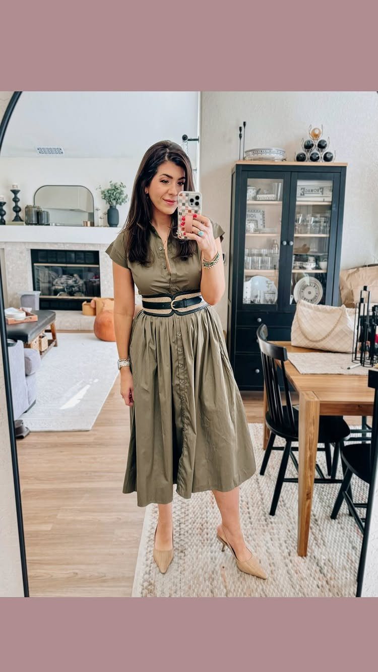 Woman in an olive green midi dress posing for a mirror selfie indoors.