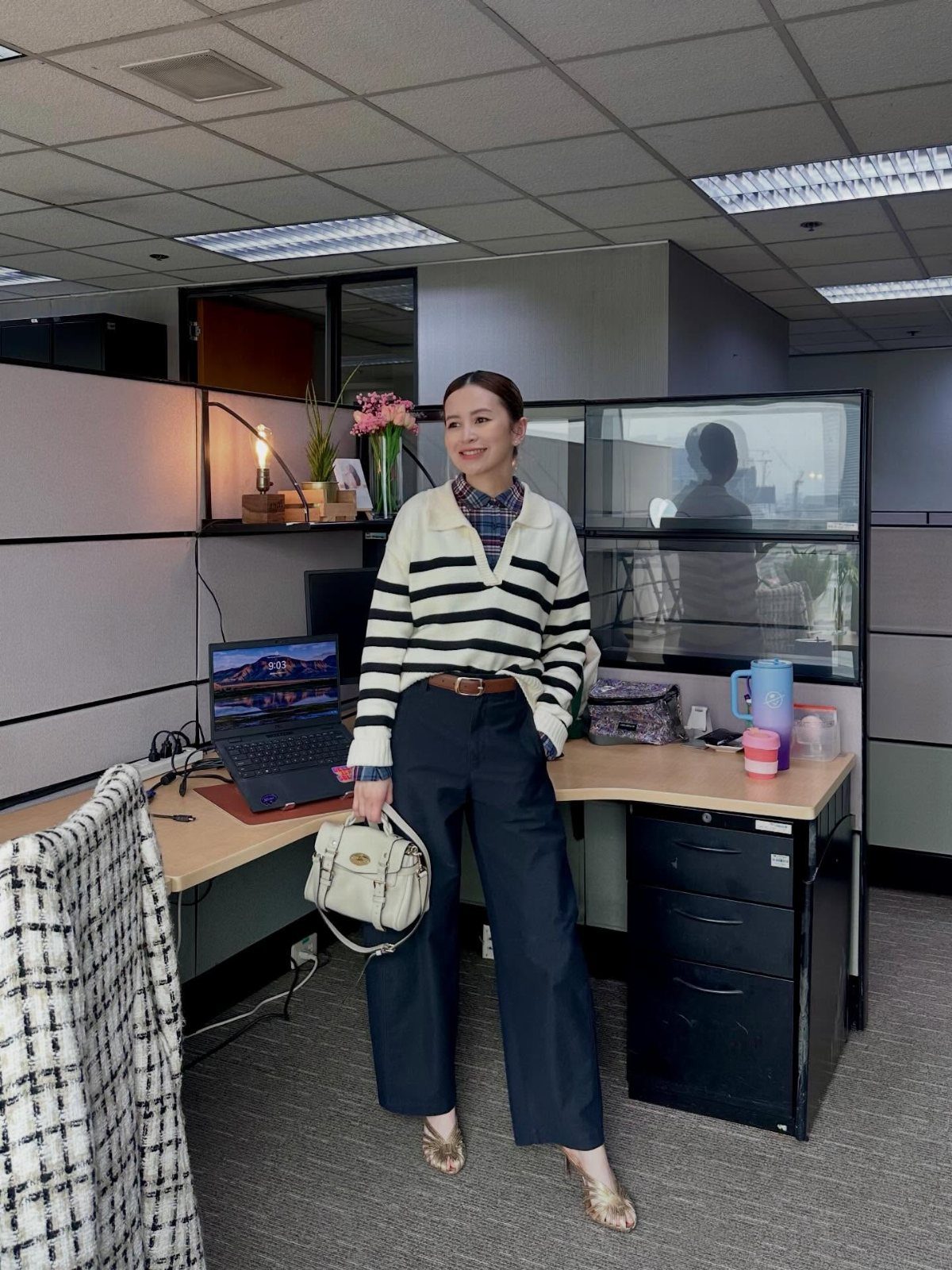 Woman in a striped sweater and navy wide-leg trousers standing in an office cubicle.