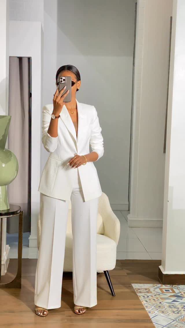 Woman in a white tailored blazer and matching wide-leg trousers posing for a mirror selfie.
