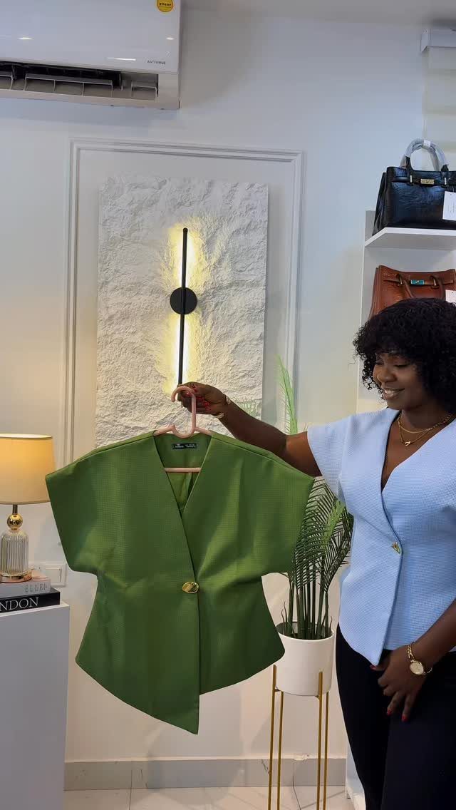 A woman holding up a bright green short-sleeved blouse on a hanger.
