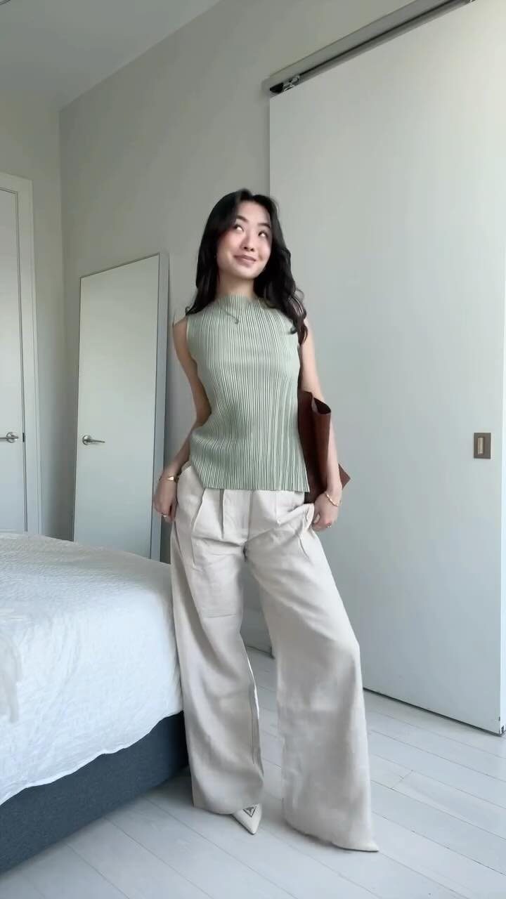 A woman wearing a green ribbed top and beige wide-leg trousers standing in a room.