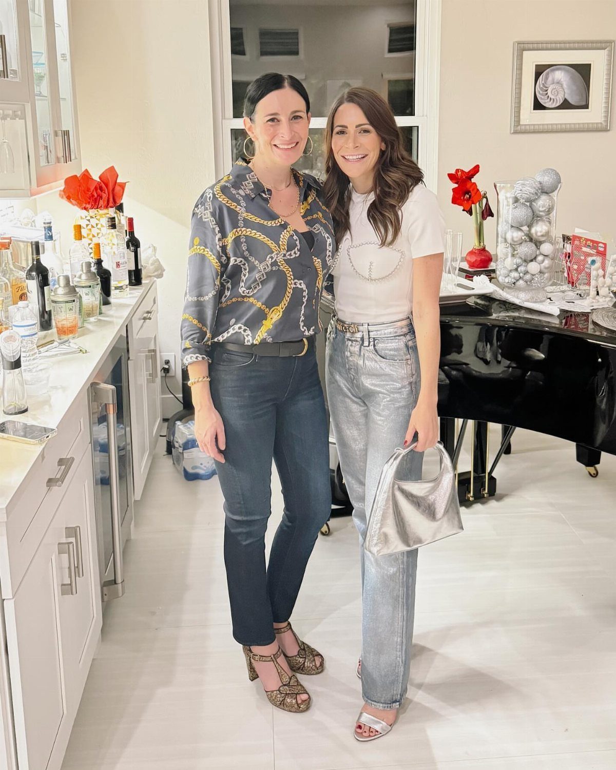 Two women posing together in a bright room wearing stylish casual outfits.