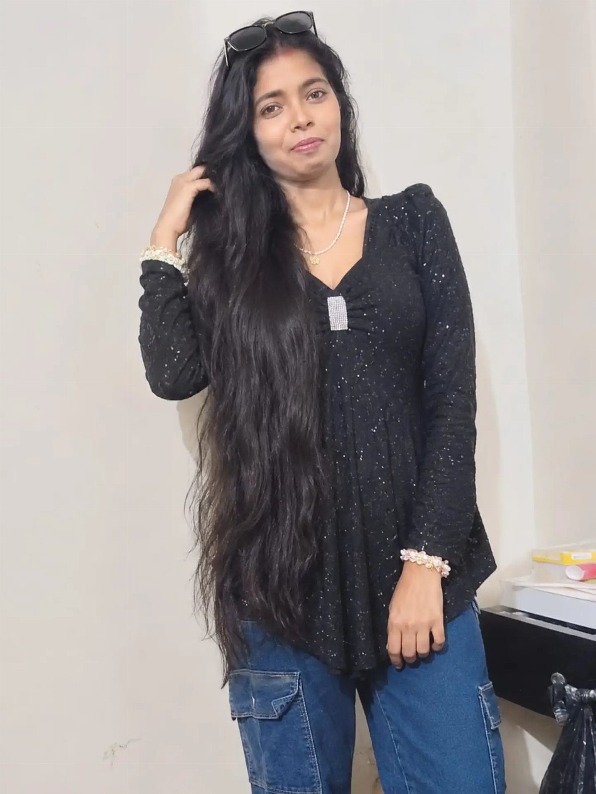 A woman posing in a black sequined top and blue denim cargo jeans.