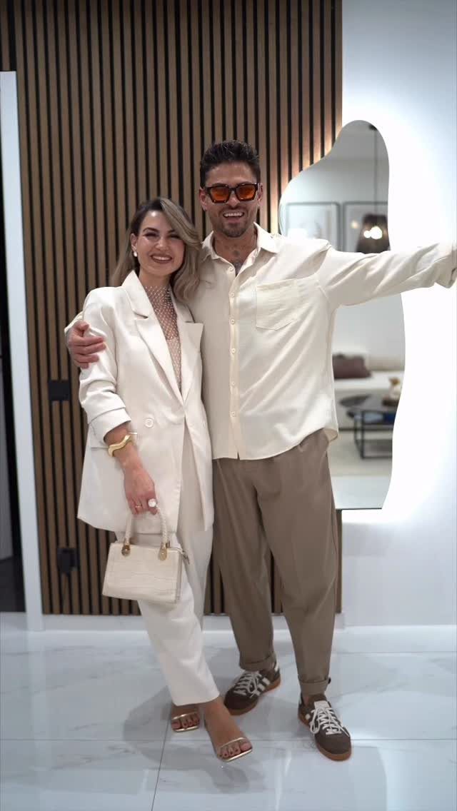 A woman in a white blazer and trousers posing with a man in a white shirt.