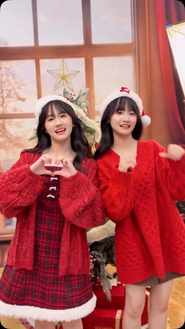 Two young women posing in festive red Christmas outfits and Santa hats.