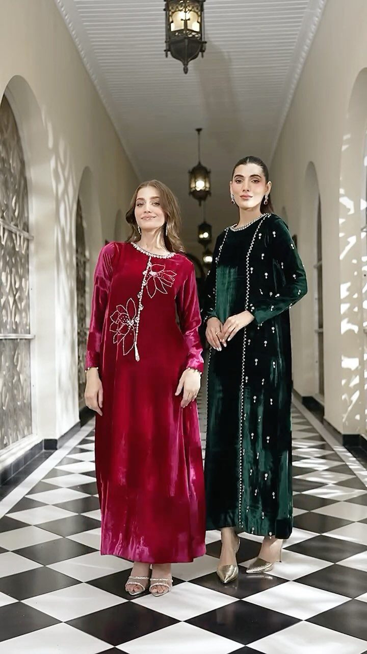Two women posing in long velvet dresses, one red with floral embroidery and one dark green with beads.