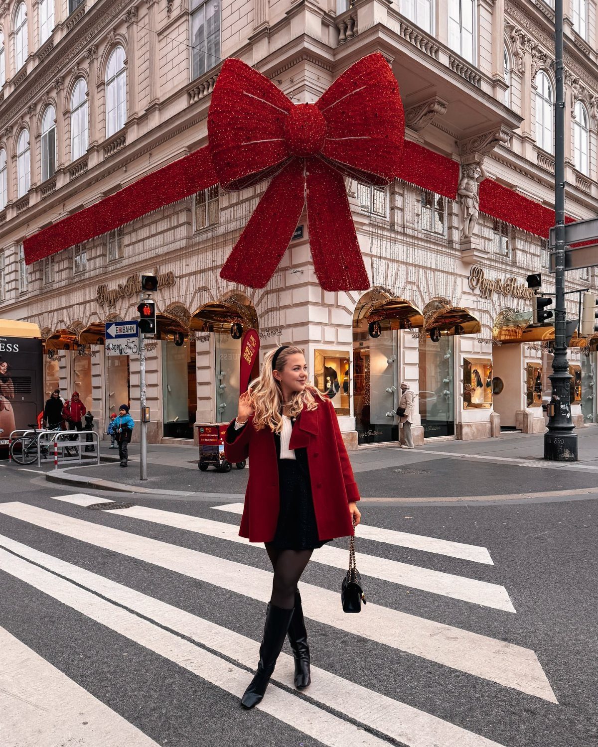 Woman in a red coat and black skirt walking across a city street crosswalk.