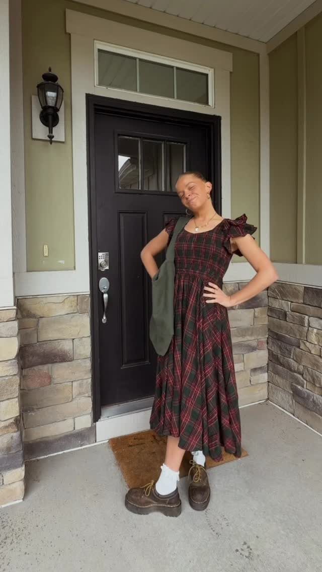 Young woman posing in a red and green plaid midi dress with brown loafers and white socks.
