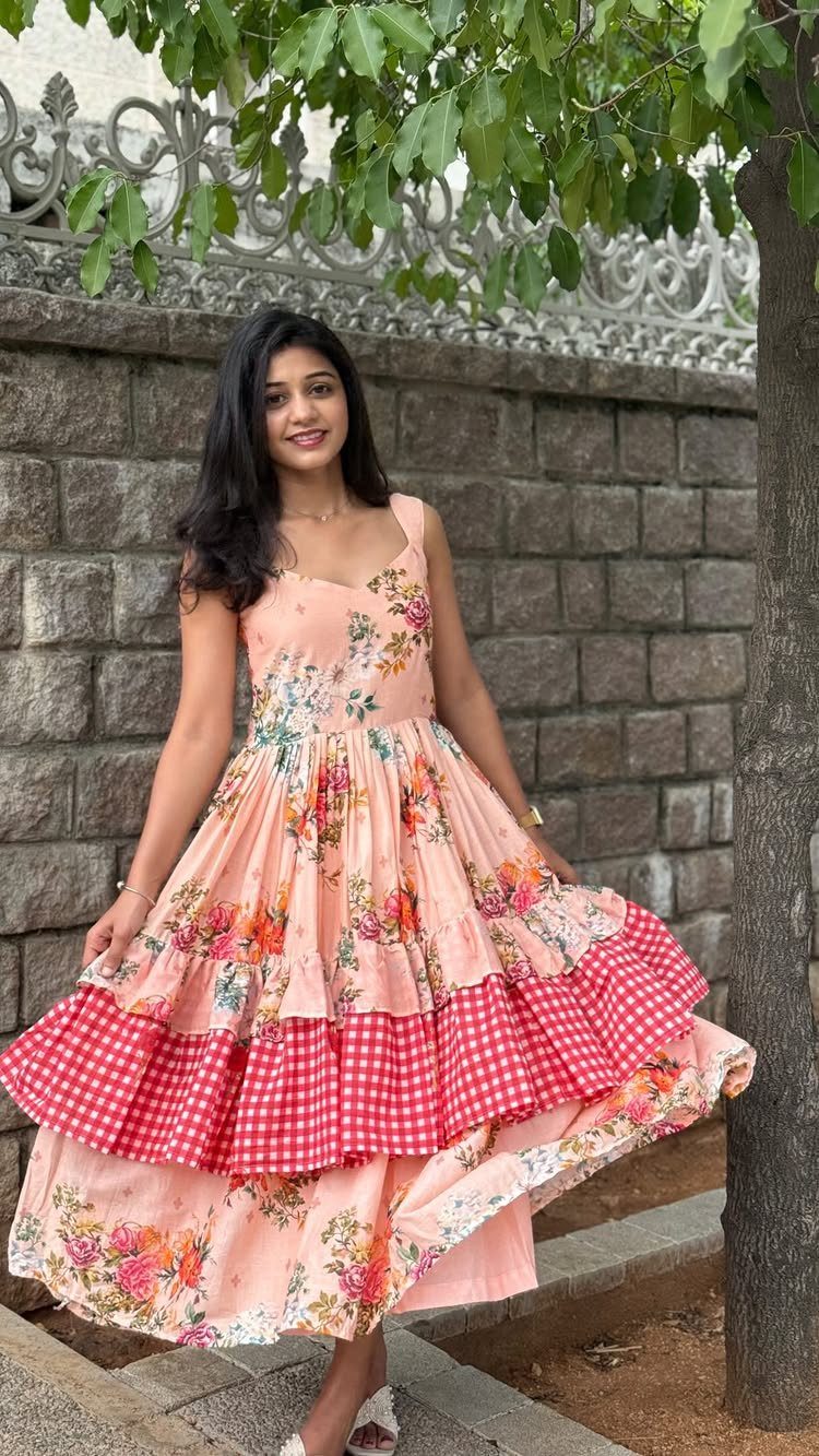 A woman posing in a peach floral midi dress with red checkered ruffles.