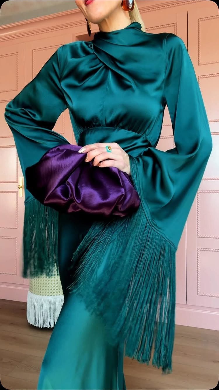 Person wearing a teal satin long-sleeved dress with fringe and holding a purple clutch.