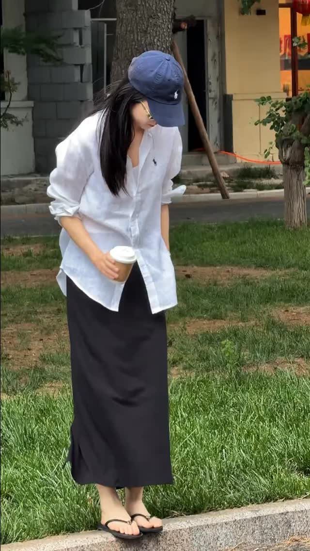 A woman in a white shirt and black skirt holding a coffee cup outdoors.