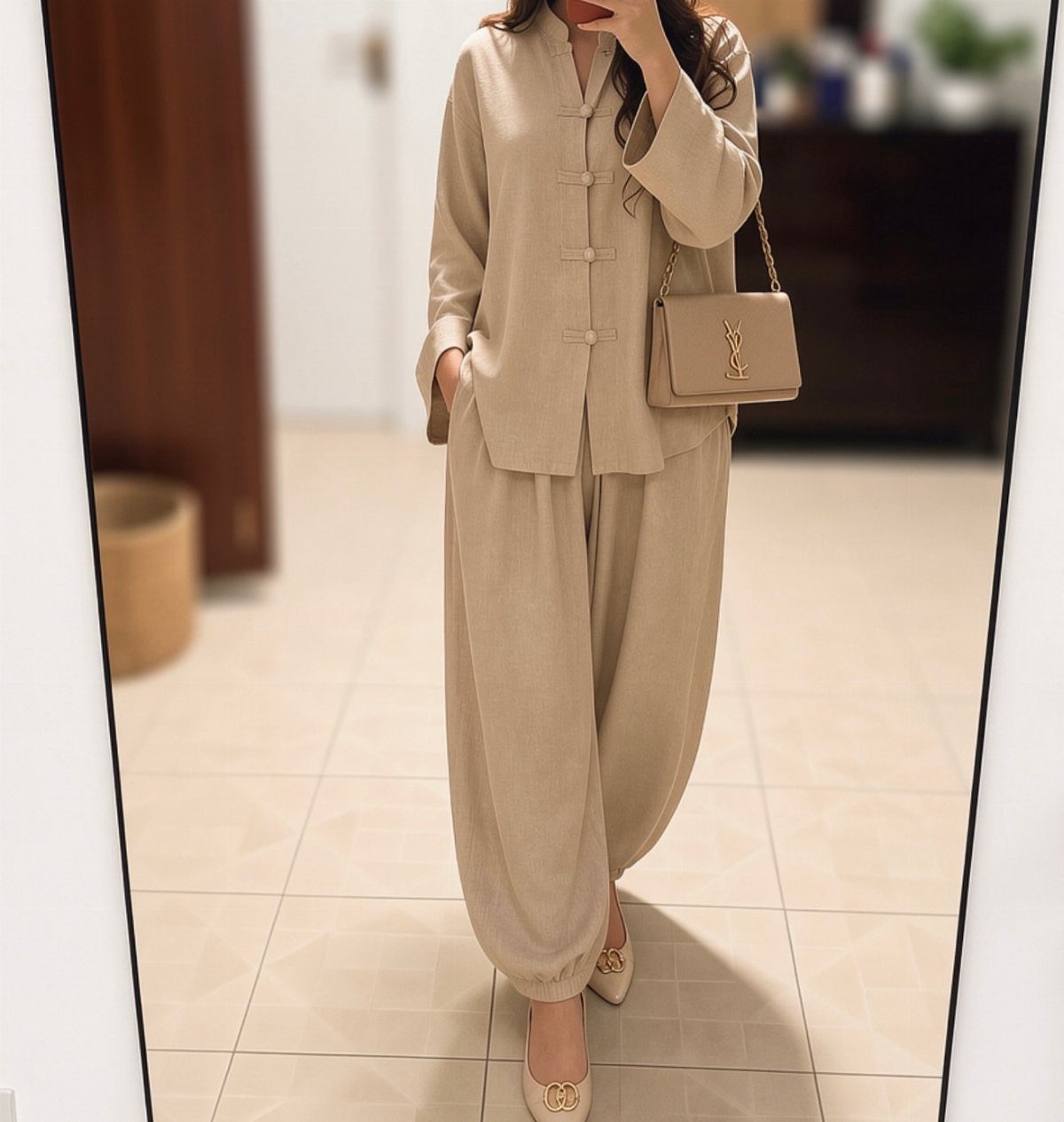 Person wearing a beige linen long-sleeved shirt and matching wide-leg trousers with a designer handbag.
