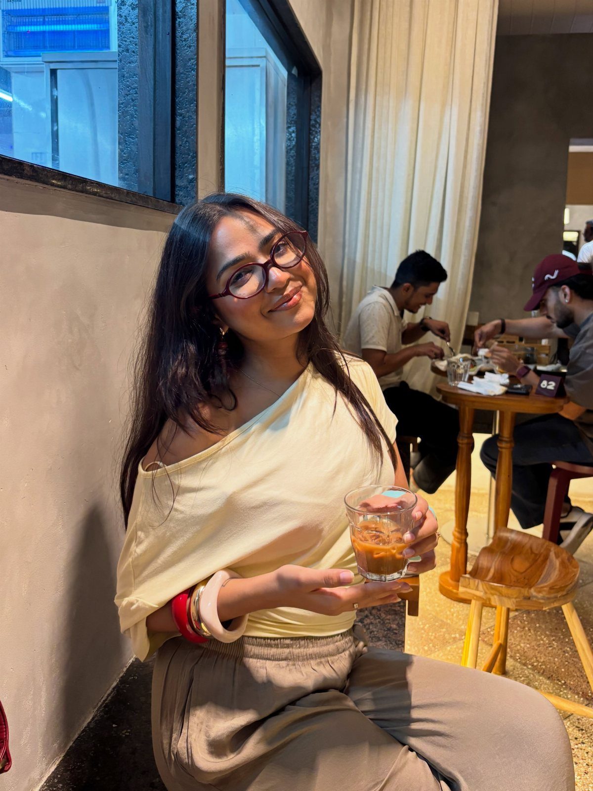 Smiling woman in an off-the-shoulder top holding a glass of coffee in a cafe.