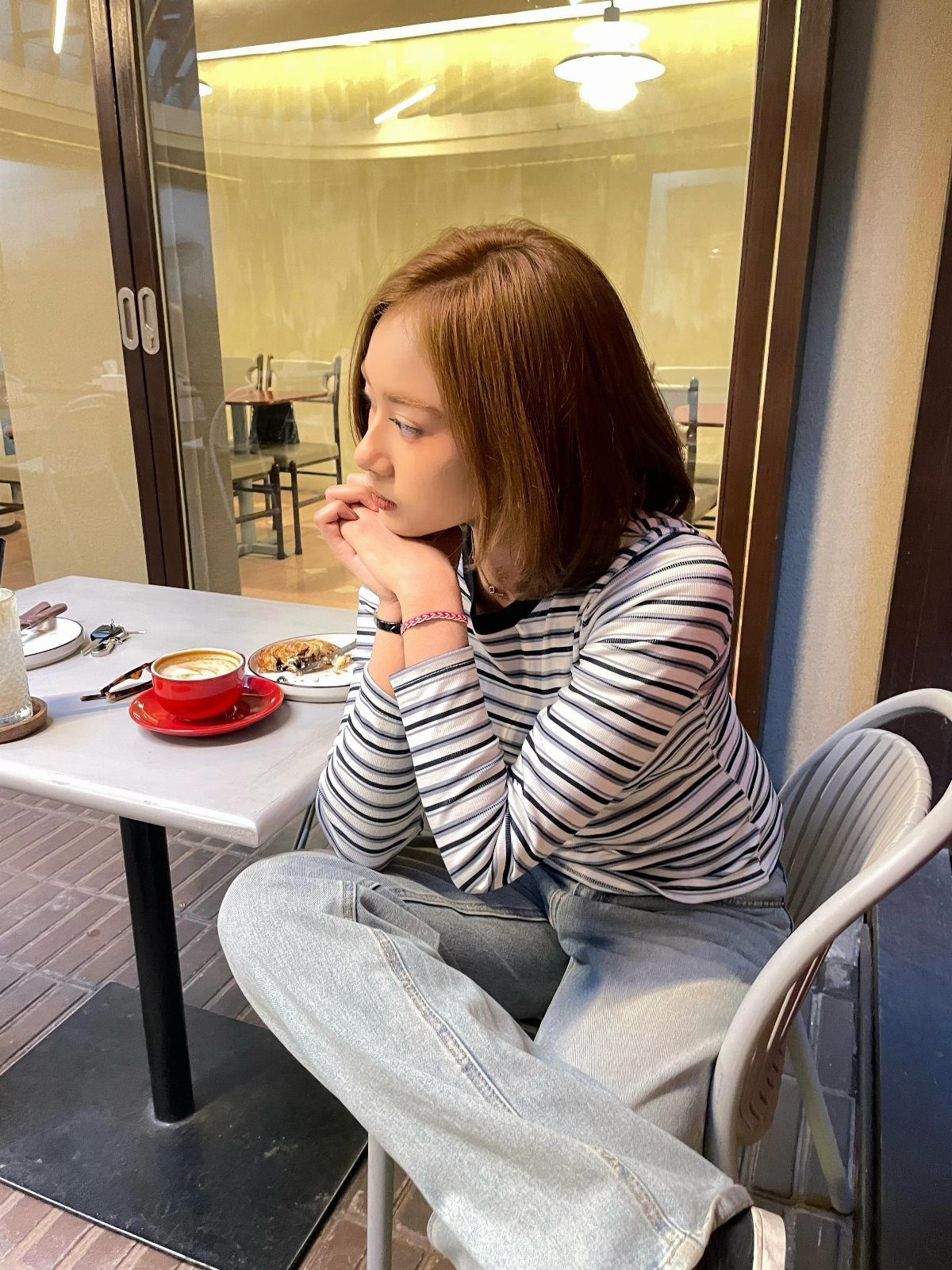 Woman in a striped long-sleeve shirt and light blue jeans sitting at a cafe table.