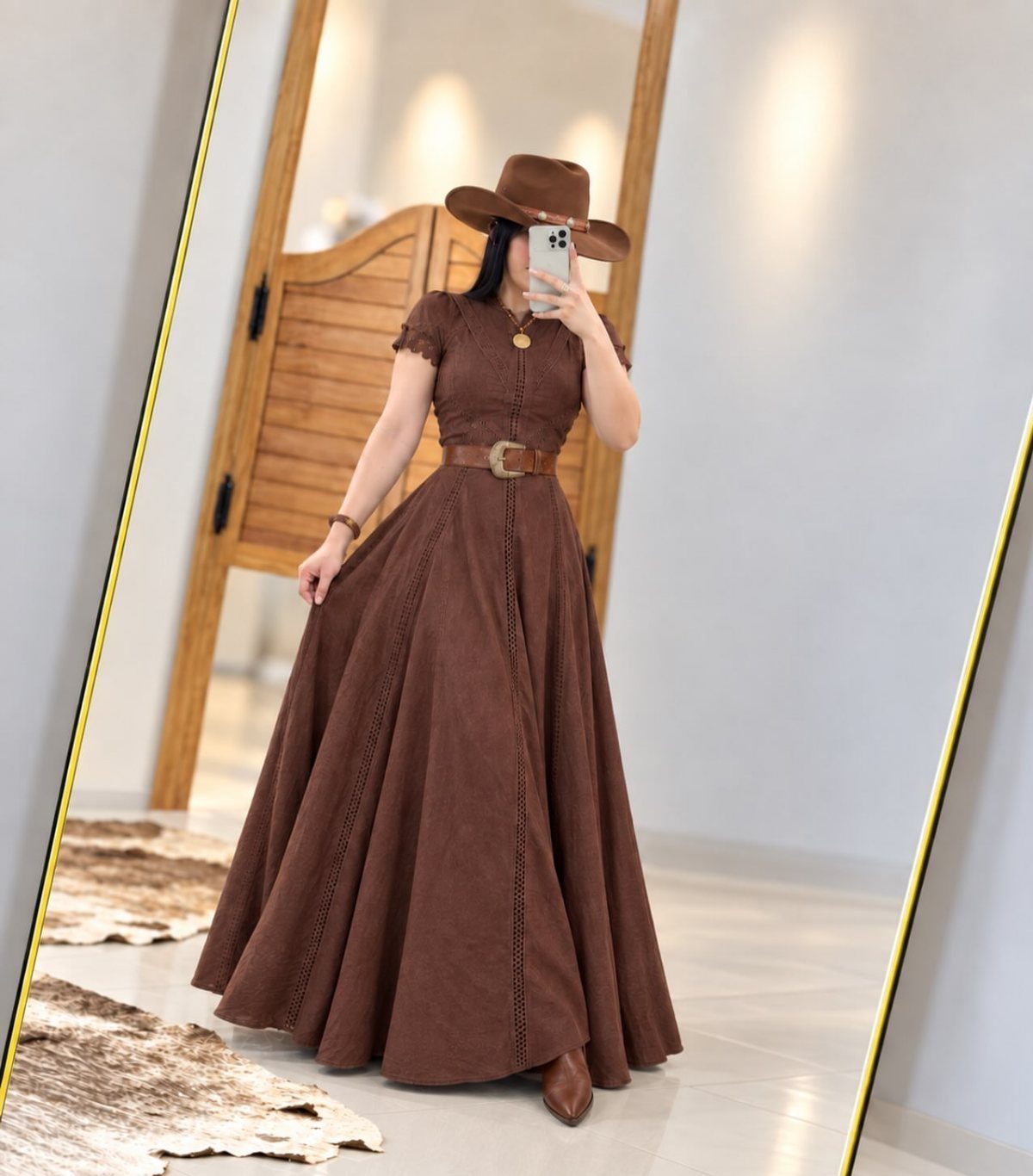 A woman in a brown flowy maxi dress and western hat taking a mirror selfie.