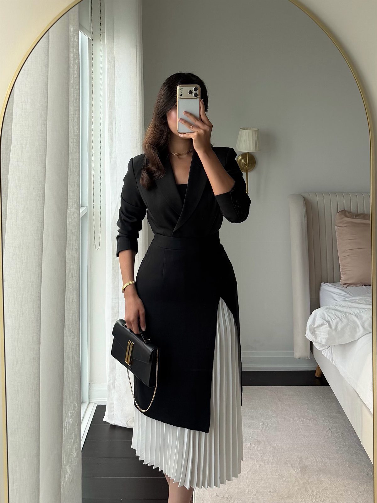 Woman in a black and white cocktail dress taking a mirror selfie in a bedroom.