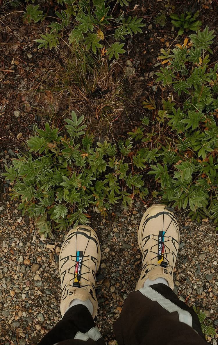 Beige and black sturdy walking shoes worn by a person standing on a gravel path.