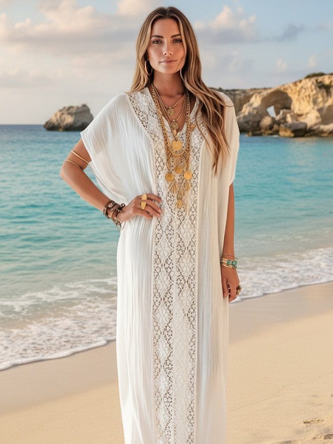 Woman in a white embroidered kaftan standing on a tropical beach with ocean waves.