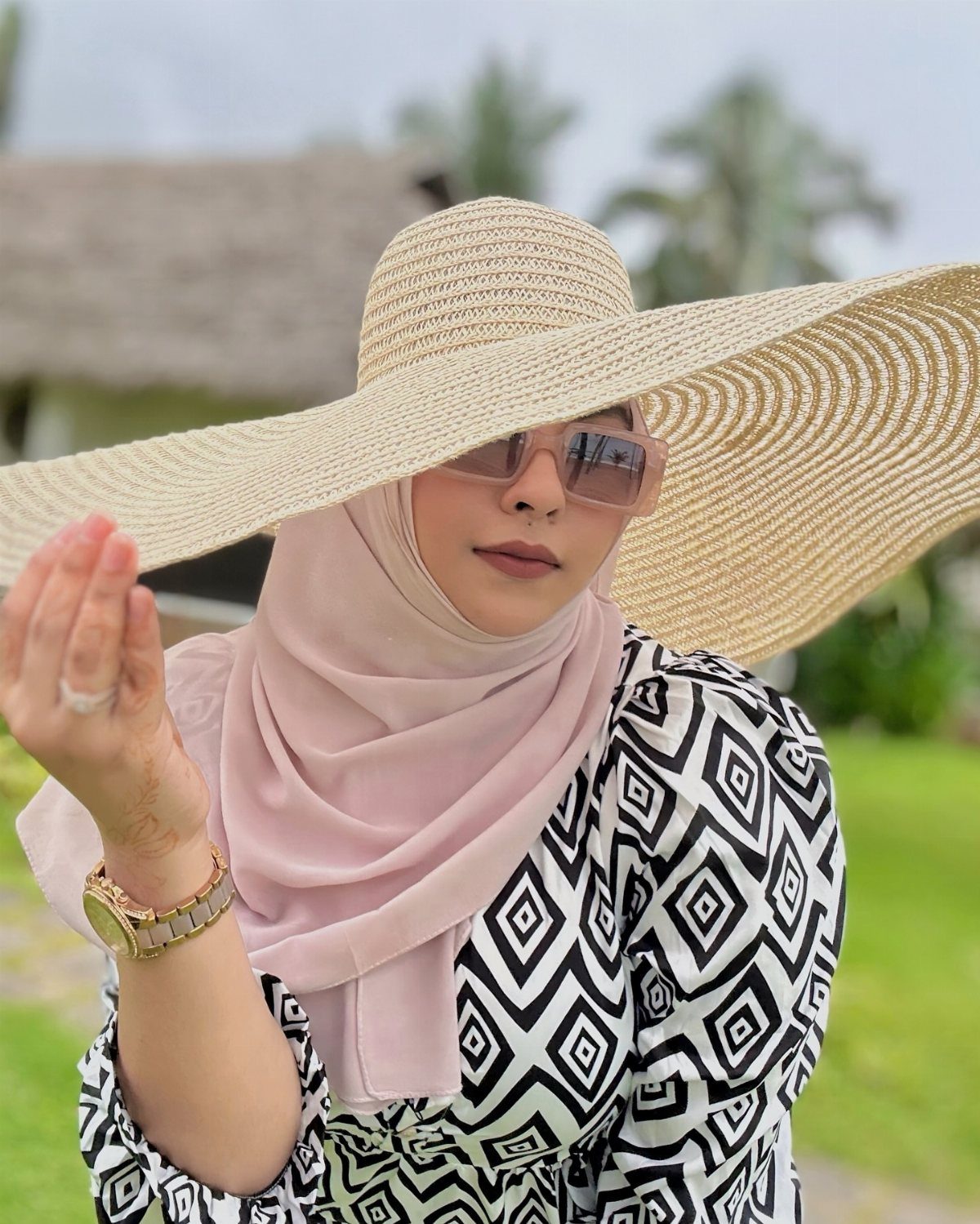 Woman wearing a large straw wide-brimmed hat and pink sunglasses outdoors.