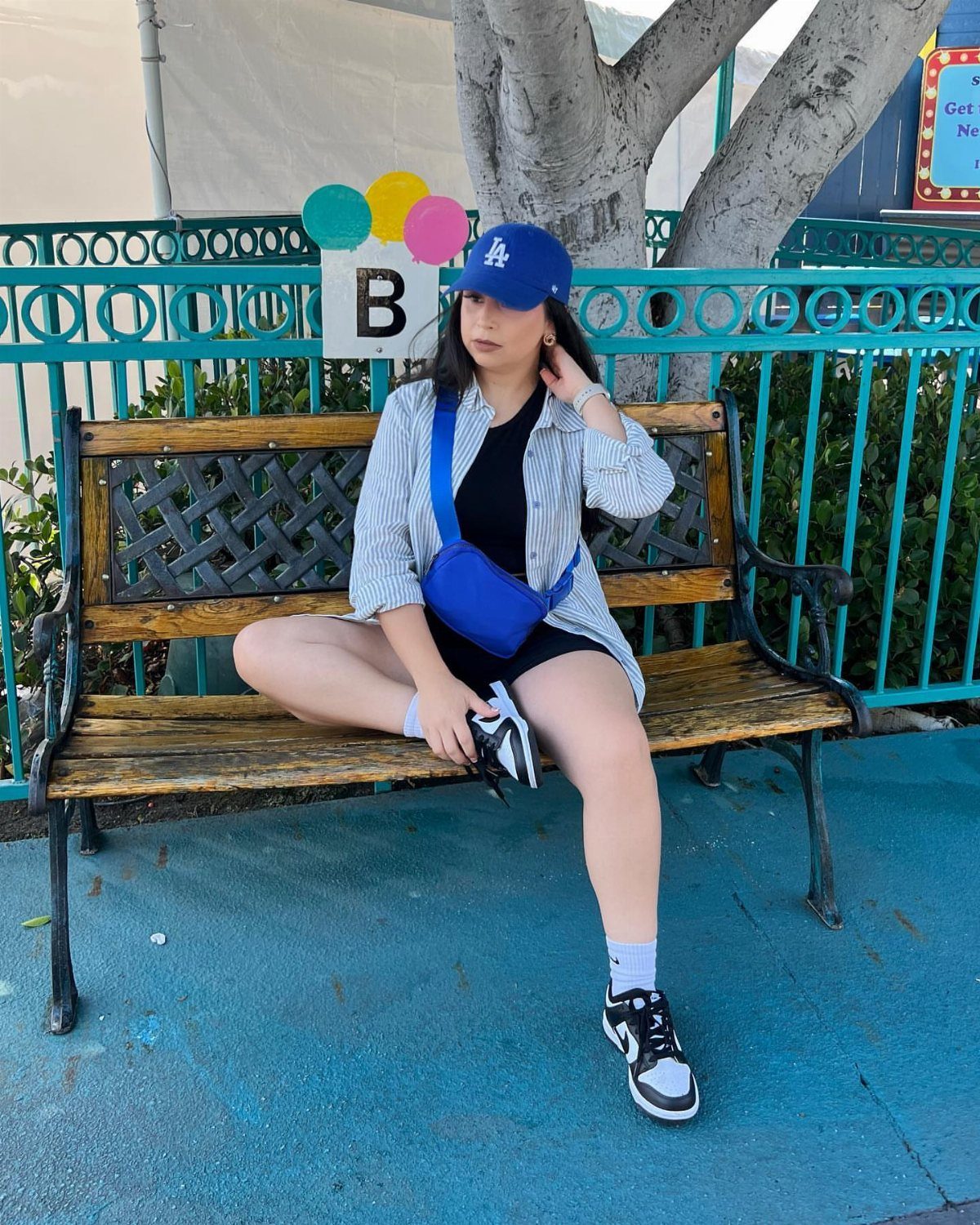 A woman in a striped shirt, blue cap, and shorts sitting on a wooden bench.