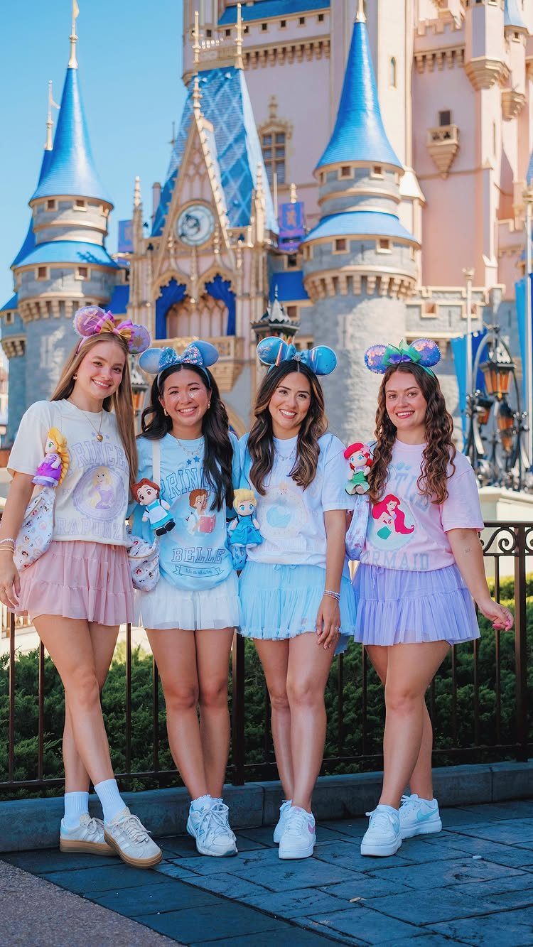 Four women wearing matching Disney graphic tees and colorful skirts posing in front of a castle.