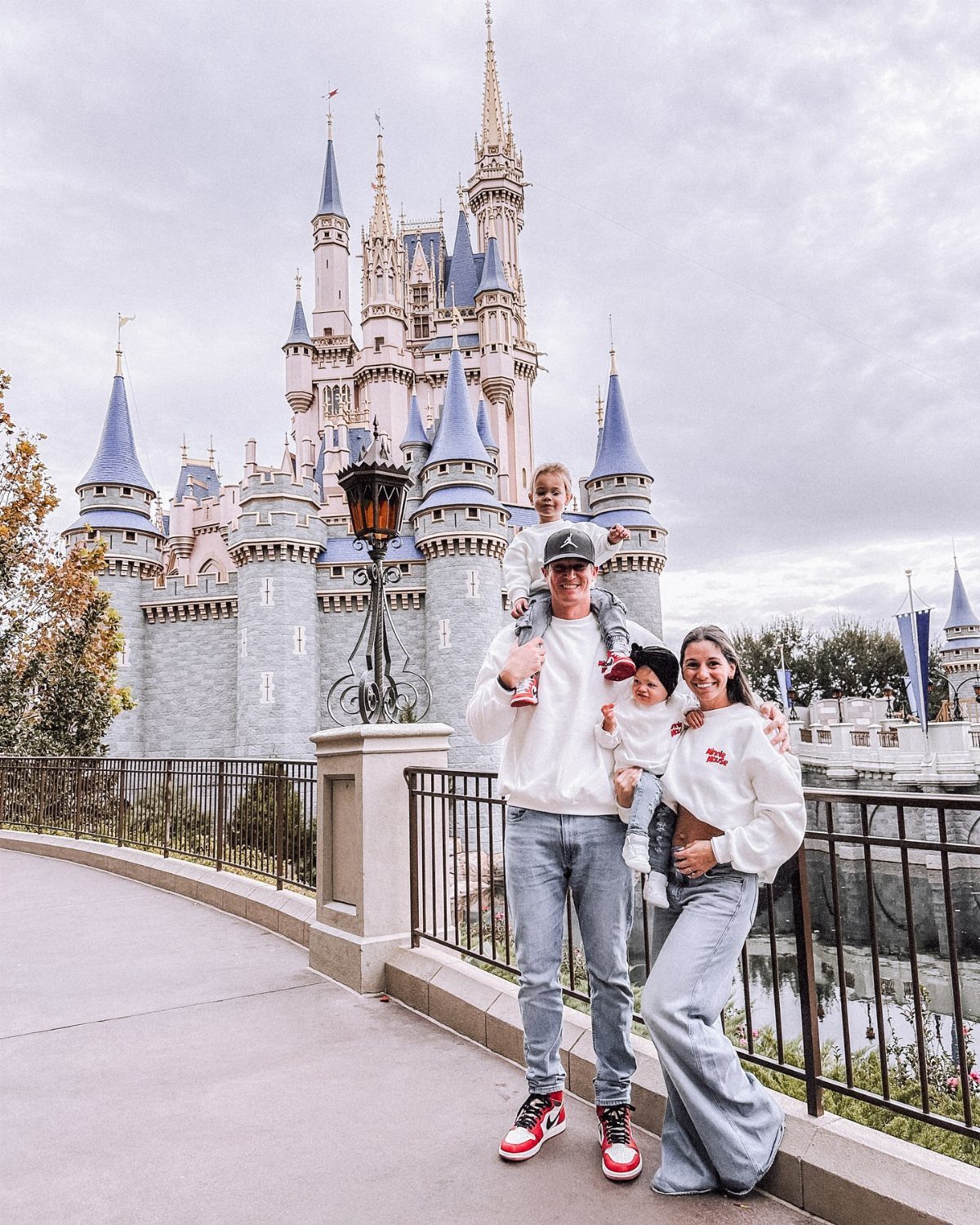 A family wearing matching white shirts poses in front of a large Disney castle.