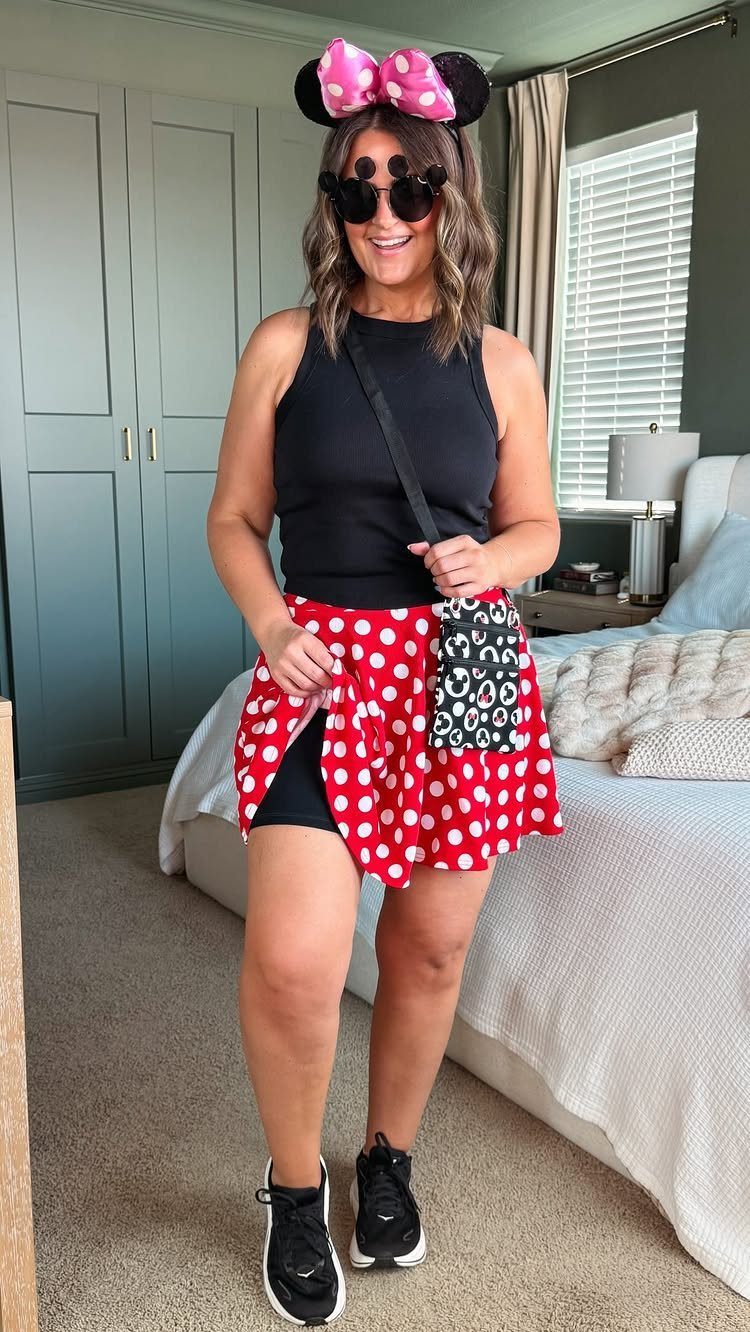 A woman wearing Minnie Mouse ears and a polka dot skirt posing in a bedroom.